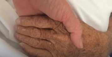Kelly Flack holds her dads hand giving him Reiki to help his transition through death